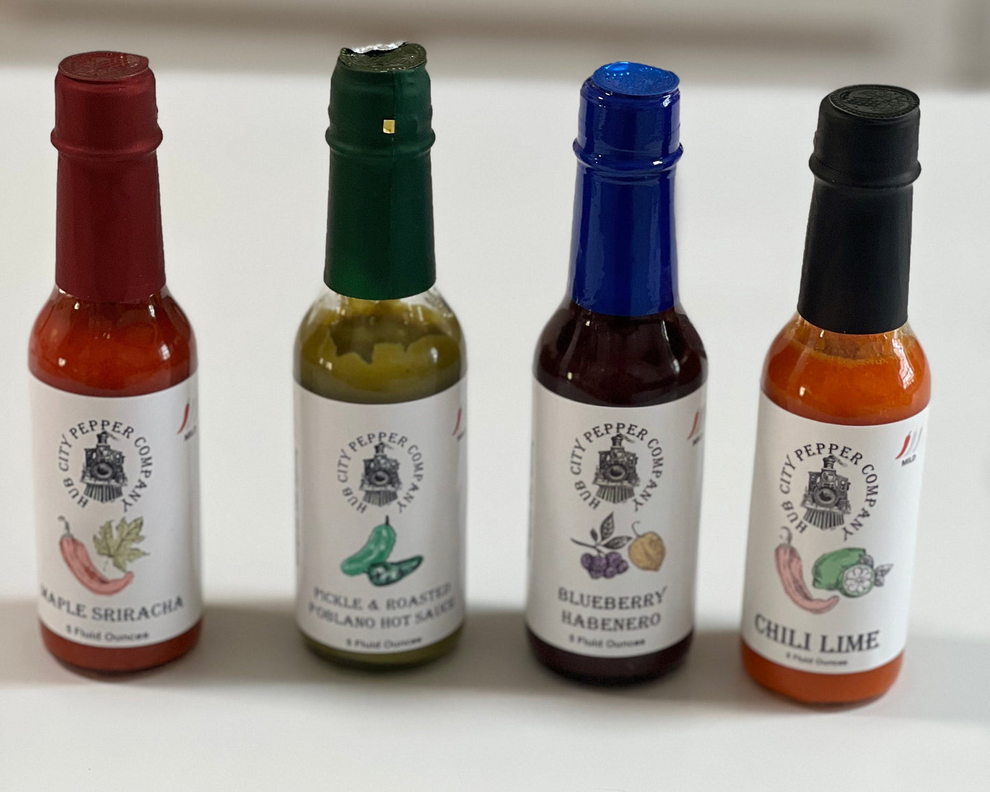 4 Pack of hot sauce flavors. Including Maple Sriracha, Pickle and Roasted Poblano, Blueberry Habenero and Chili Lime flavors. all images are from the front and above.