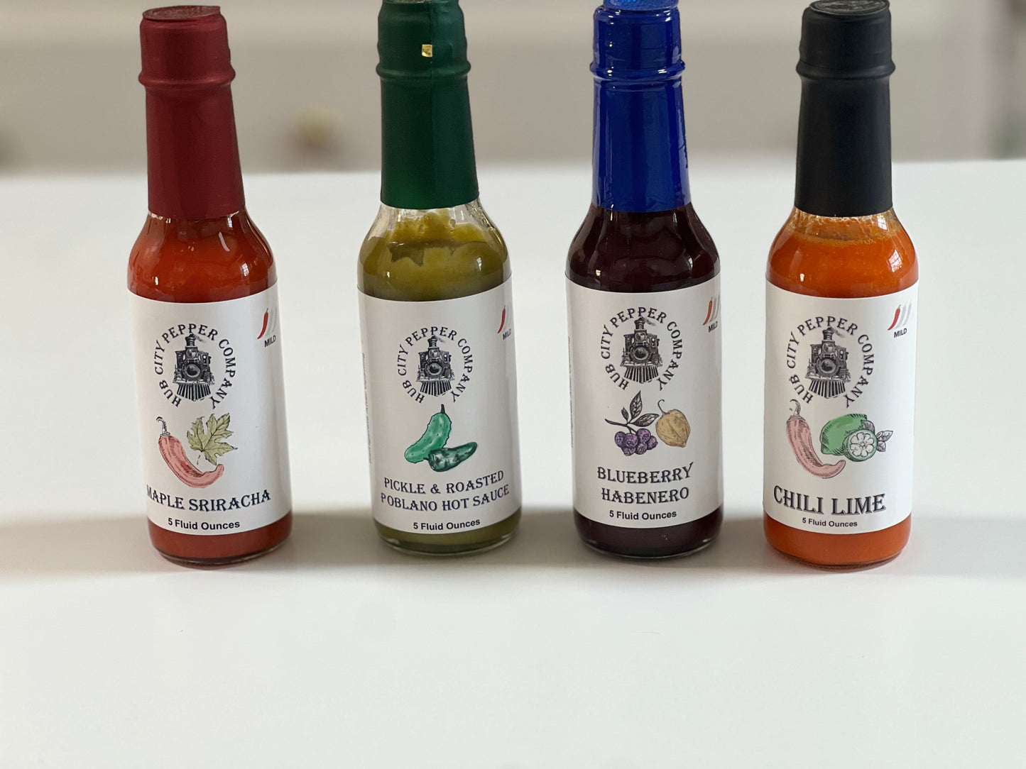 4 Pack of hot sauce flavors. Including Maple Sriracha, Pickle and Roasted Poblano, Blueberry Habenero and Chili Lime flavors. all images are from the front with spacing. 