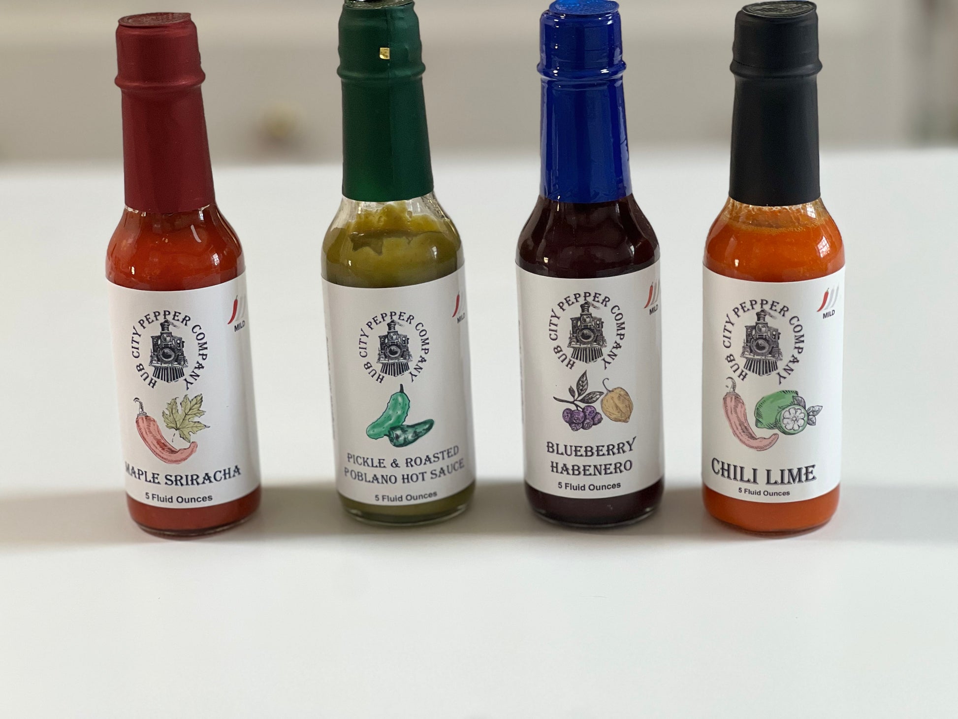 4 Pack of hot sauce flavors. Including Maple Sriracha, Pickle and Roasted Poblano, Blueberry Habenero and Chili Lime flavors. all images are from the front of all 4 hot sauces.