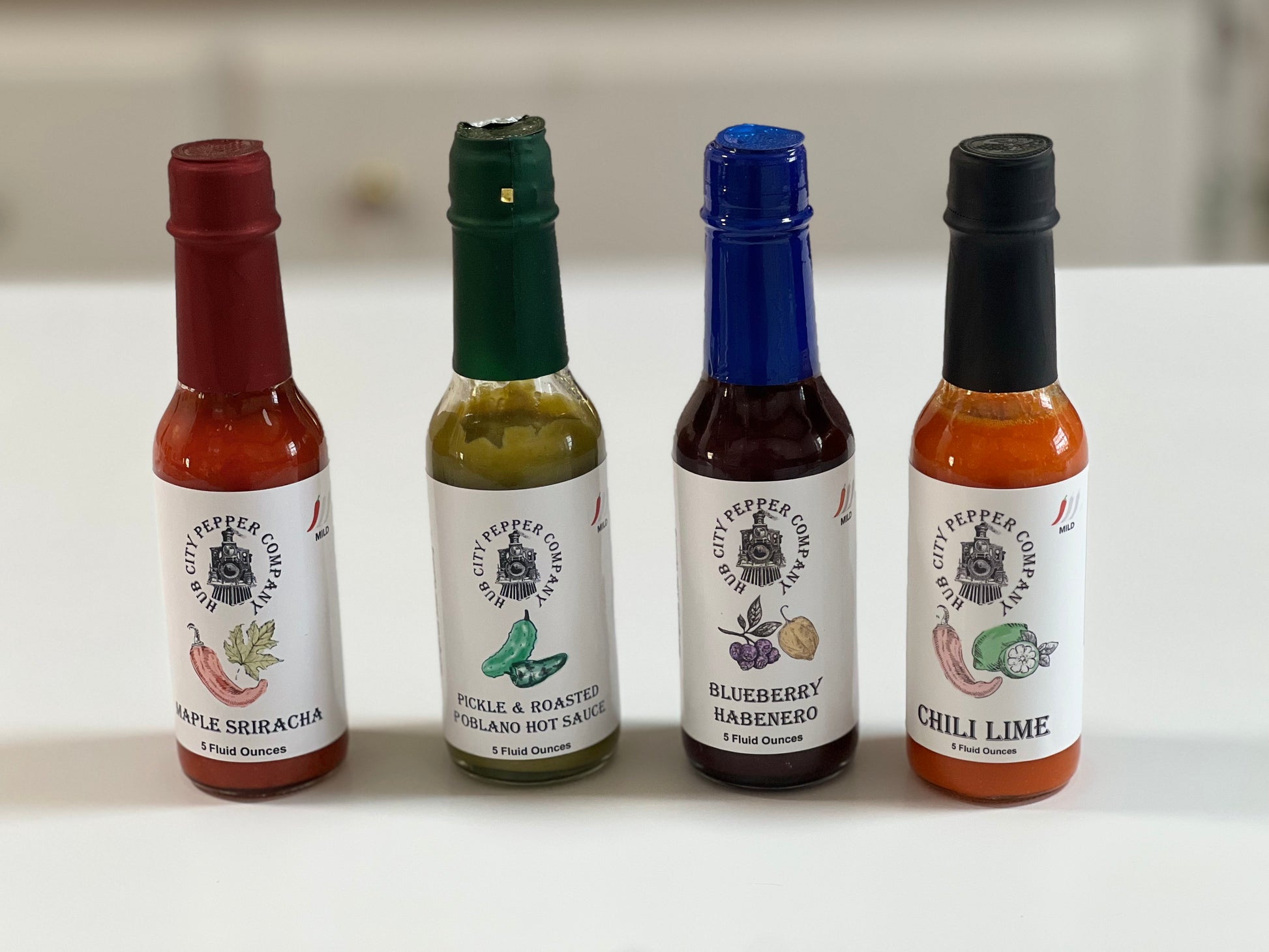 4 Pack of hot sauce flavors. Including Maple Sriracha, Pickle and Roasted Poblano, Blueberry Habenero and Chili Lime flavors. all images are from the front. Spicy.